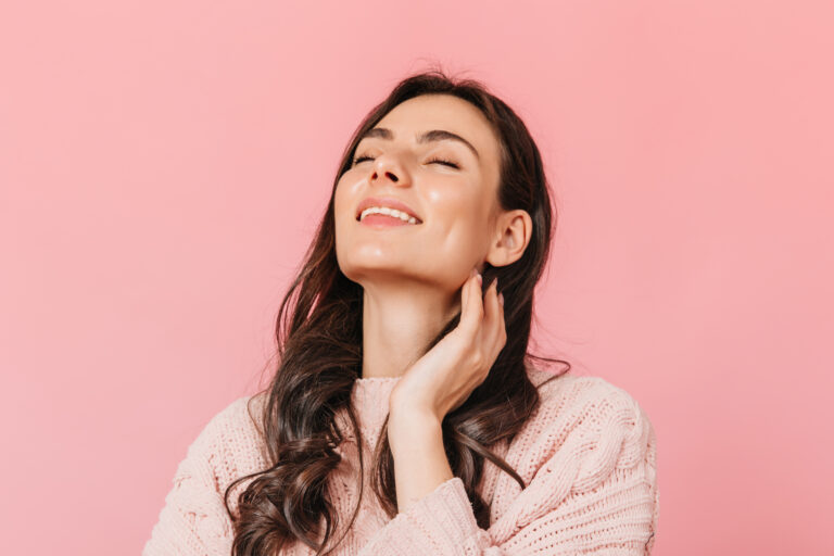 Joyful girl with wavy dark hair poses with smile and closed eyes on isolated background